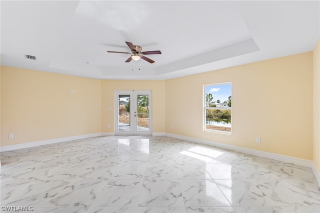 tiled empty room with a raised ceiling, french doors, and ceiling fan