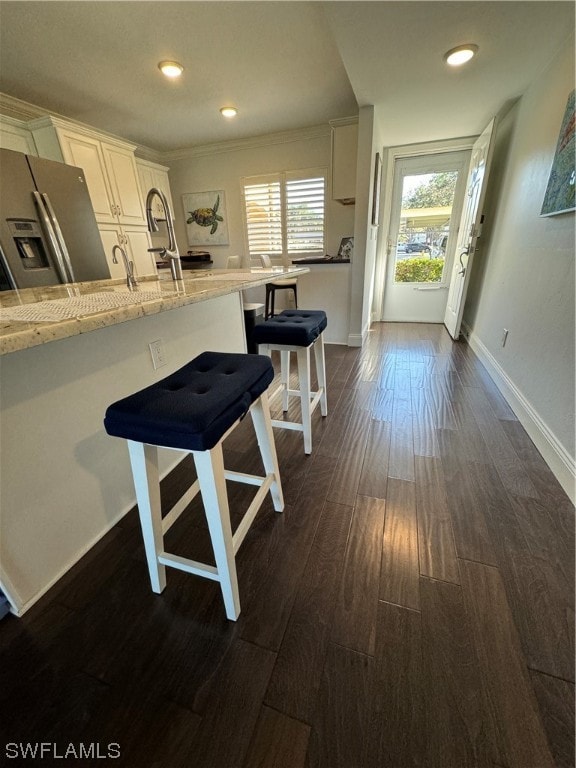 kitchen with stainless steel fridge with ice dispenser, white cabinets, a breakfast bar, dark wood-type flooring, and light stone countertops