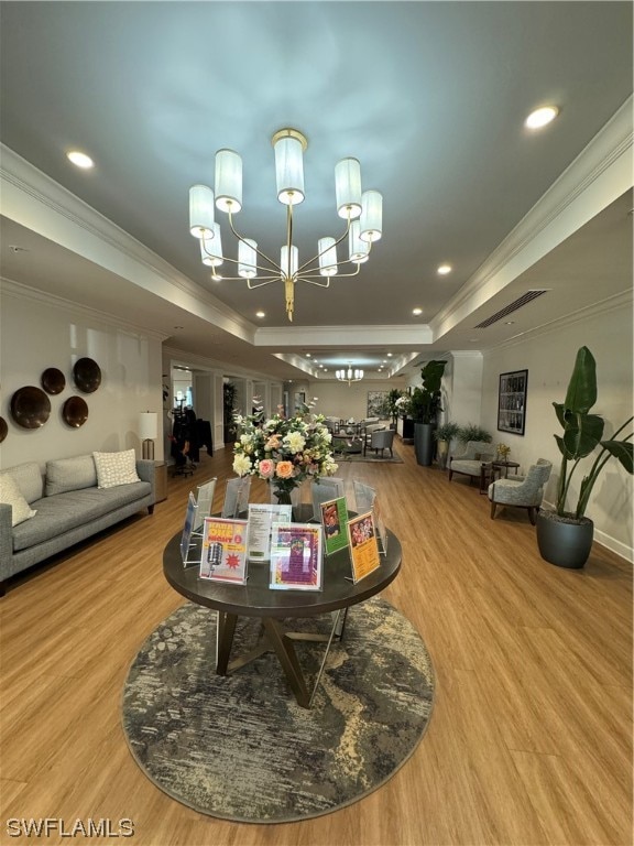 rec room featuring a notable chandelier, light hardwood / wood-style floors, a tray ceiling, and ornamental molding