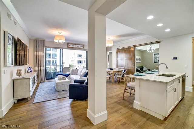 living room with a barn door, light hardwood / wood-style floors, sink, and an inviting chandelier