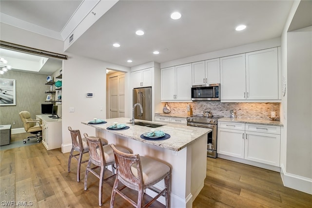 kitchen with light hardwood / wood-style flooring, appliances with stainless steel finishes, white cabinetry, a kitchen island with sink, and sink