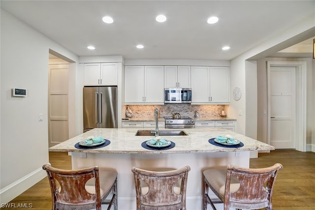 kitchen with light stone countertops, dark hardwood / wood-style floors, high end appliances, an island with sink, and white cabinets