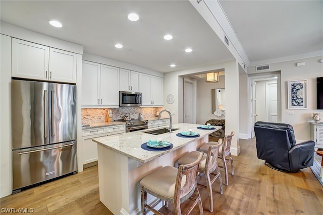 kitchen featuring a kitchen island with sink, sink, appliances with stainless steel finishes, light hardwood / wood-style floors, and white cabinetry