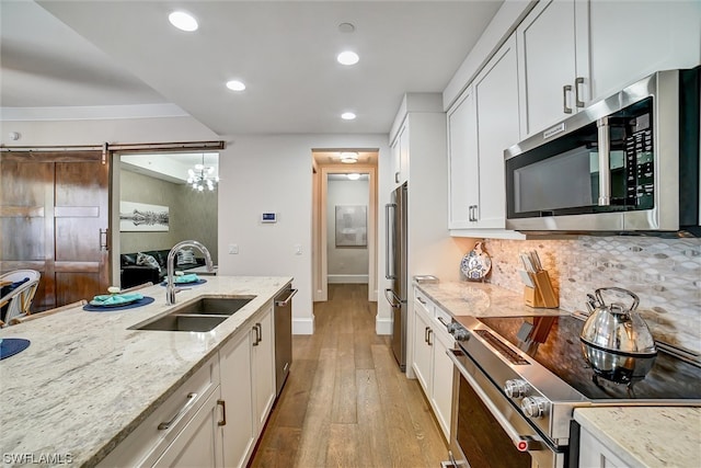 kitchen with sink, appliances with stainless steel finishes, backsplash, white cabinetry, and light wood-type flooring