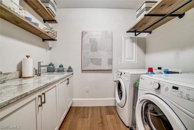 clothes washing area featuring washing machine and clothes dryer, cabinets, sink, and light wood-type flooring