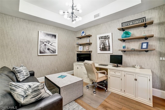 office area with an inviting chandelier, a raised ceiling, and light wood-type flooring