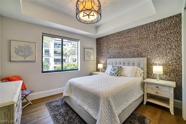 bedroom featuring a raised ceiling and dark wood-type flooring