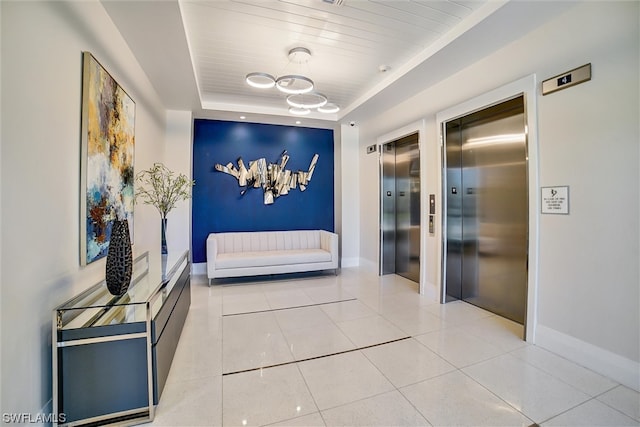 bedroom featuring light tile floors, a notable chandelier, elevator, and a tray ceiling