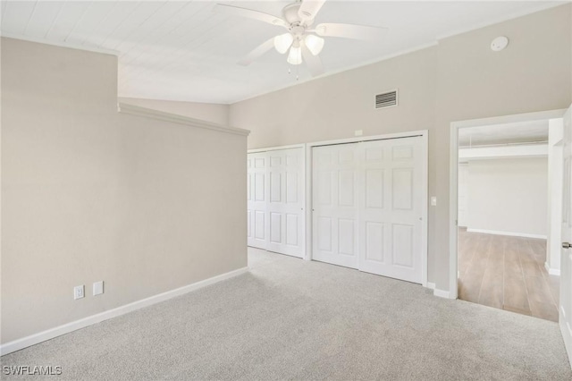 unfurnished bedroom featuring light carpet, ceiling fan, lofted ceiling, and multiple closets