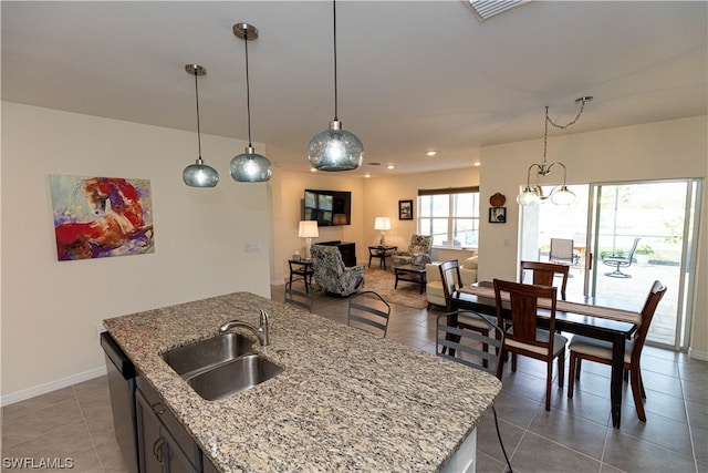 kitchen featuring light stone counters, a kitchen island with sink, sink, a chandelier, and dark tile floors