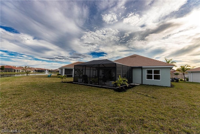 back of house featuring a lawn, a tile roof, a lanai, and stucco siding