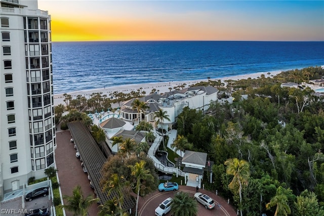 aerial view at dusk featuring a water view and a beach view