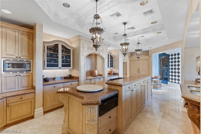 kitchen featuring stainless steel microwave, light brown cabinets, pendant lighting, a tray ceiling, and a kitchen island