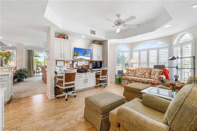 living room with plenty of natural light, built in desk, ceiling fan, and a raised ceiling