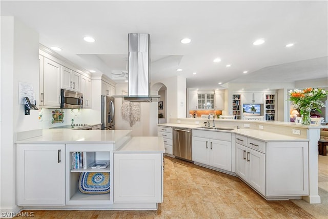 kitchen with white cabinets, appliances with stainless steel finishes, sink, island range hood, and kitchen peninsula