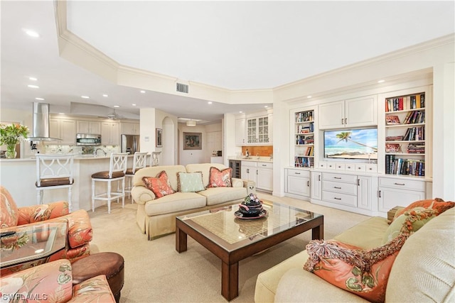 carpeted living room with built in shelves, crown molding, and wine cooler