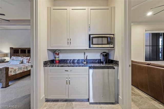 kitchen featuring light colored carpet, appliances with stainless steel finishes, crown molding, white cabinetry, and dark stone countertops