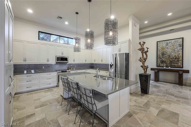 kitchen featuring dark stone counters, a kitchen island with sink, appliances with stainless steel finishes, and white cabinetry