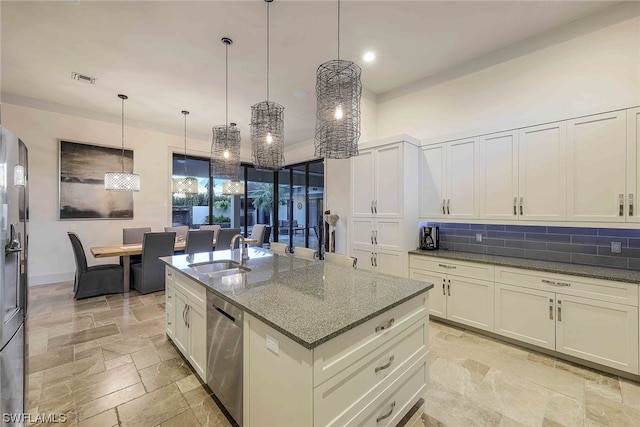 kitchen featuring pendant lighting, dark stone counters, a center island with sink, dishwasher, and sink