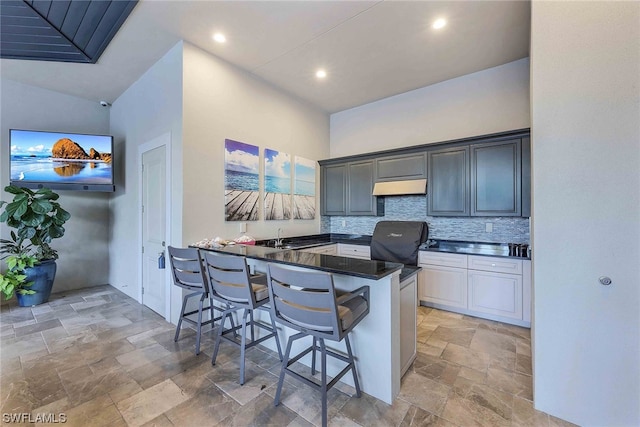 kitchen featuring kitchen peninsula, backsplash, a kitchen bar, light tile floors, and dark stone countertops