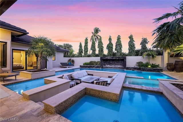 pool at dusk with a patio, an in ground hot tub, and an outdoor living space with a fire pit