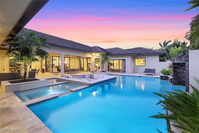 pool at dusk featuring a patio area and an in ground hot tub