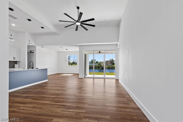 unfurnished living room with ceiling fan, a towering ceiling, a water view, dark hardwood / wood-style floors, and sink