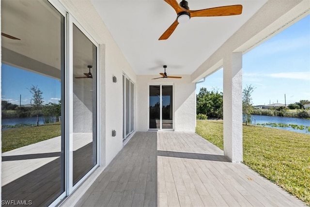 wooden deck featuring a lawn, ceiling fan, and a water view