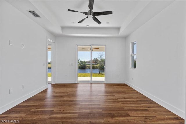 unfurnished room with a water view, a raised ceiling, ceiling fan, and dark hardwood / wood-style flooring