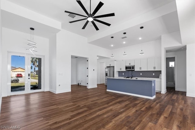 kitchen featuring an island with sink, hanging light fixtures, stainless steel appliances, dark wood-type flooring, and white cabinetry