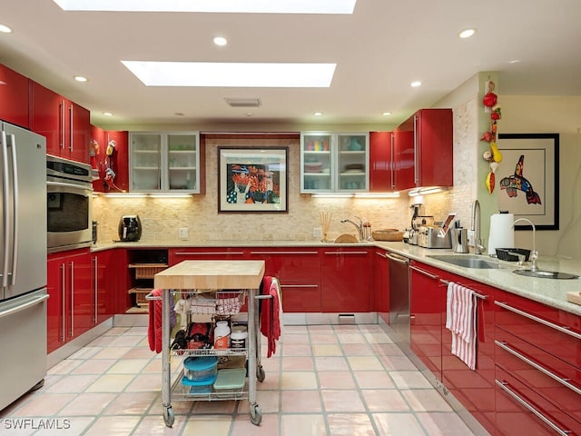 kitchen featuring decorative backsplash, modern cabinets, glass insert cabinets, stainless steel appliances, and a sink