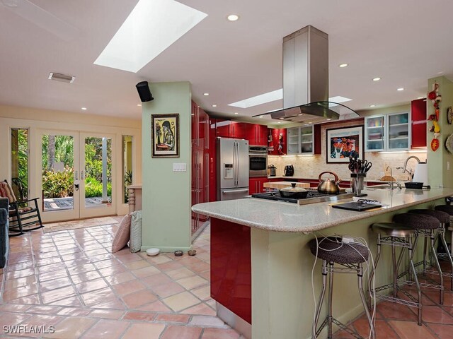 kitchen with a skylight, glass insert cabinets, appliances with stainless steel finishes, a peninsula, and island exhaust hood