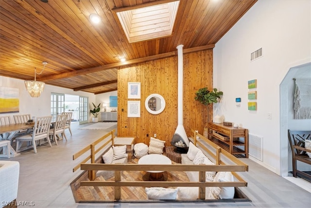 living room featuring beamed ceiling, wooden ceiling, wooden walls, a notable chandelier, and a skylight