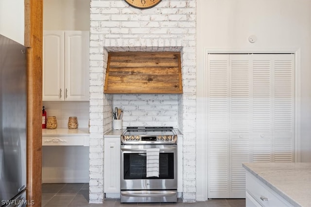 kitchen with brick wall, appliances with stainless steel finishes, white cabinetry, and dark tile floors