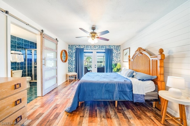 bedroom featuring a barn door, french doors, wood-type flooring, and ceiling fan