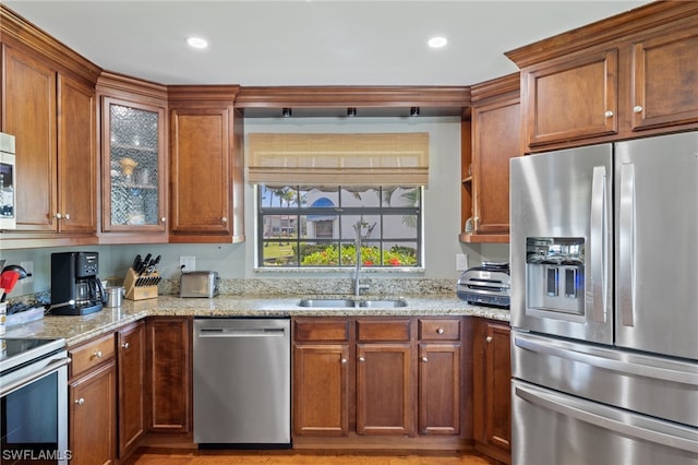 kitchen with appliances with stainless steel finishes, light stone countertops, sink, and light wood-type flooring