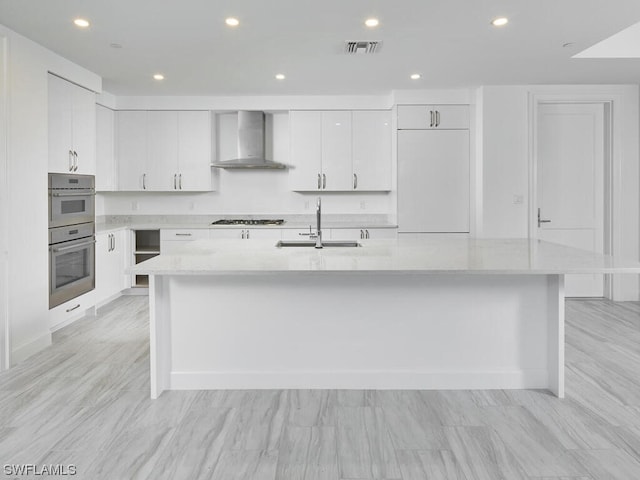 kitchen featuring appliances with stainless steel finishes, sink, white cabinets, a kitchen island with sink, and wall chimney exhaust hood