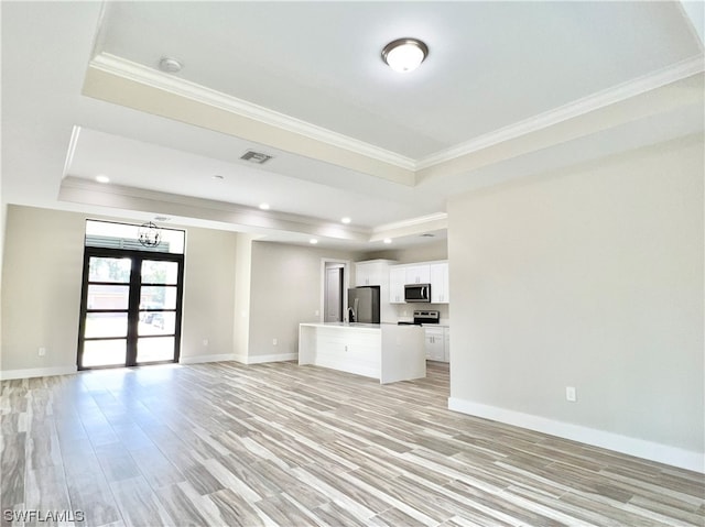 unfurnished living room featuring french doors, a raised ceiling, ornamental molding, a chandelier, and light hardwood / wood-style flooring