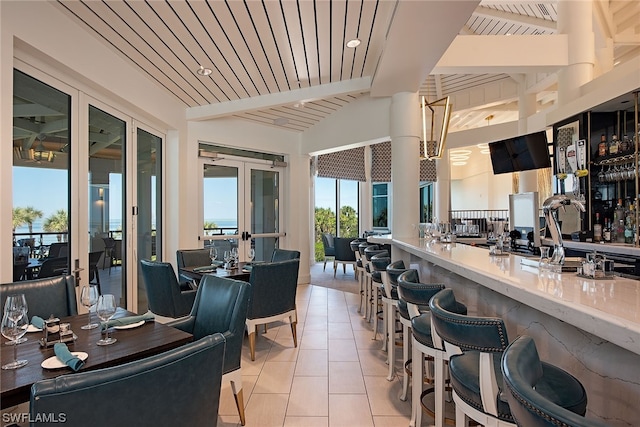 interior space featuring light tile floors, beam ceiling, french doors, and bar