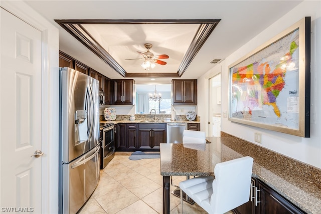 kitchen featuring ceiling fan with notable chandelier, stainless steel appliances, dark stone countertops, a raised ceiling, and ornamental molding