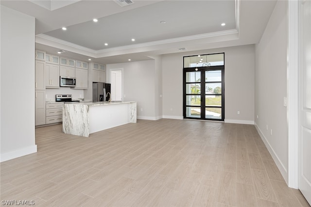 kitchen with light wood-type flooring, stainless steel appliances, a raised ceiling, light stone counters, and an island with sink