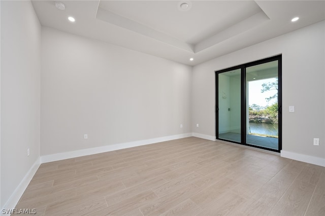 unfurnished room with light hardwood / wood-style flooring and a tray ceiling