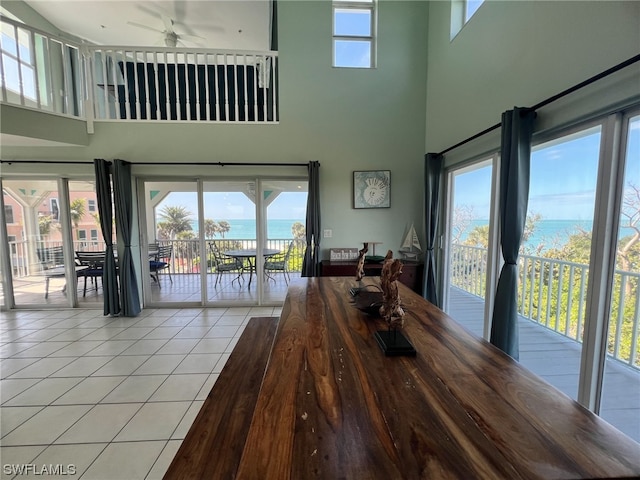 unfurnished dining area with a water view, light tile floors, ceiling fan, and a towering ceiling