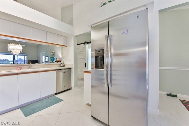 kitchen with a barn door, light tile patterned flooring, pendant lighting, white cabinets, and appliances with stainless steel finishes