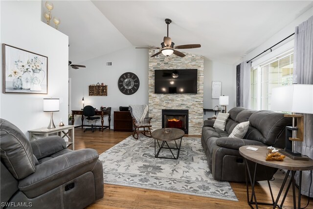 living room with a stone fireplace, ceiling fan, vaulted ceiling, and wood-type flooring