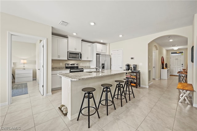 kitchen featuring light tile flooring, a kitchen bar, a center island with sink, and appliances with stainless steel finishes