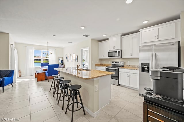 kitchen with an island with sink, a breakfast bar, appliances with stainless steel finishes, white cabinetry, and light stone counters