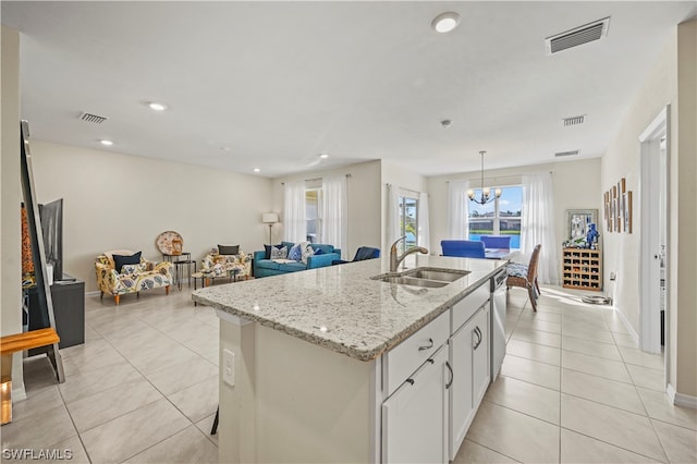 kitchen with light stone countertops, white cabinetry, sink, a center island with sink, and a chandelier