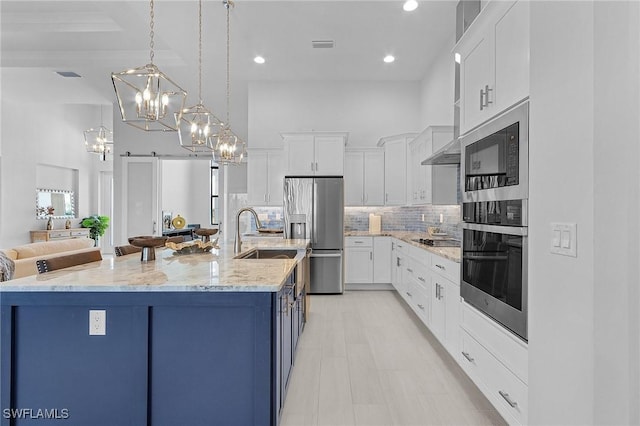 kitchen with a barn door, white cabinetry, a large island with sink, and appliances with stainless steel finishes