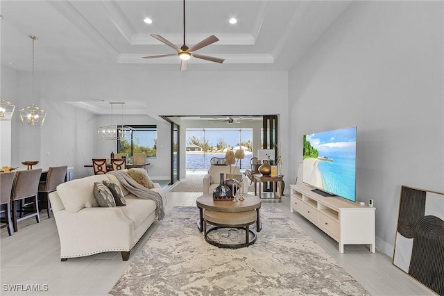 living room with ceiling fan with notable chandelier, a towering ceiling, and a raised ceiling